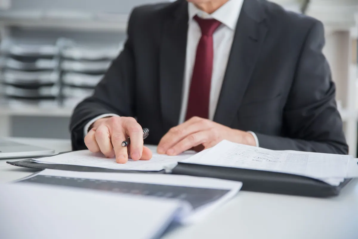 A printed document being read closely with a pen in hand